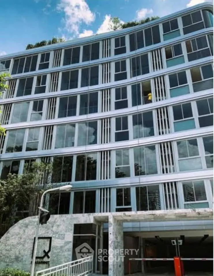 Modern apartment building with sleek glass facade and lush greenery, ideal urban living.