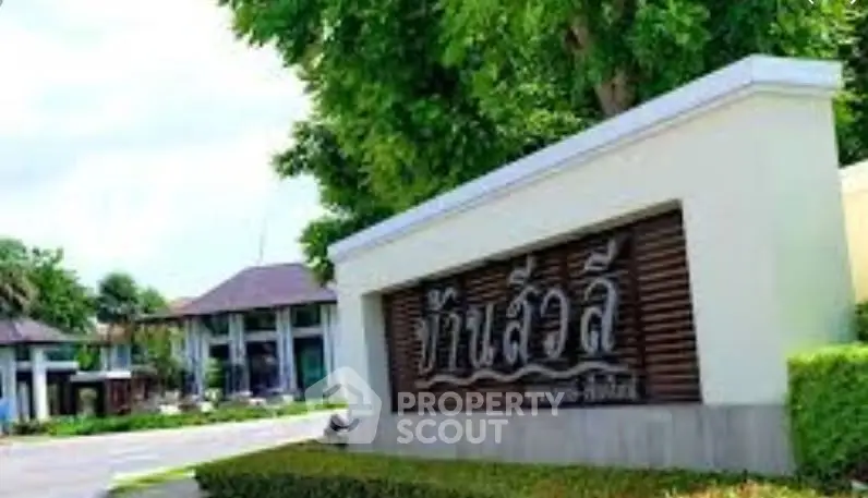 Elegant entrance of a modern residential complex with lush greenery and stylish signage.