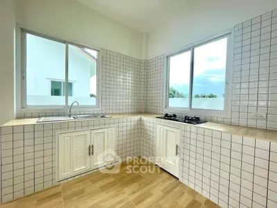 Modern kitchen with tiled walls, gas stove, and large windows offering natural light.