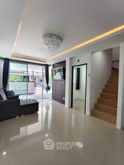 Modern living room with elegant chandelier and staircase, featuring sleek tile flooring and large windows.