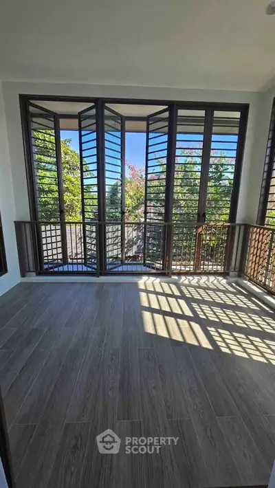 Spacious balcony with large windows offering a scenic view of lush greenery, perfect for relaxation.
