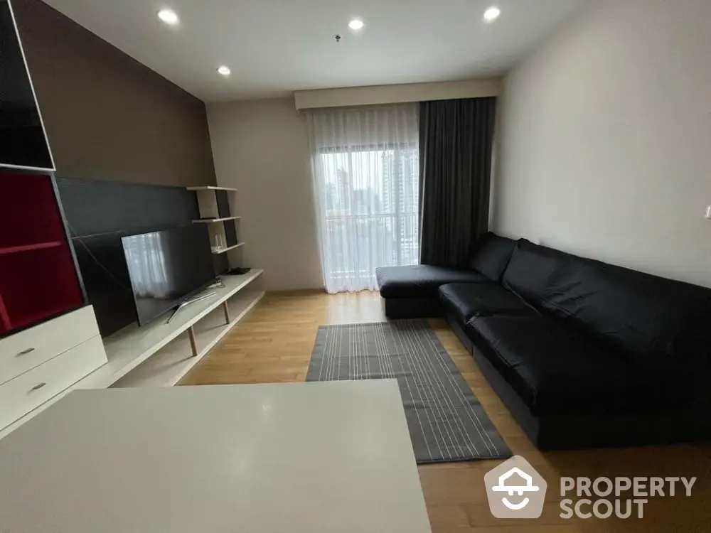 Modern living room with sleek black sofa and large TV, featuring a city view from the window.