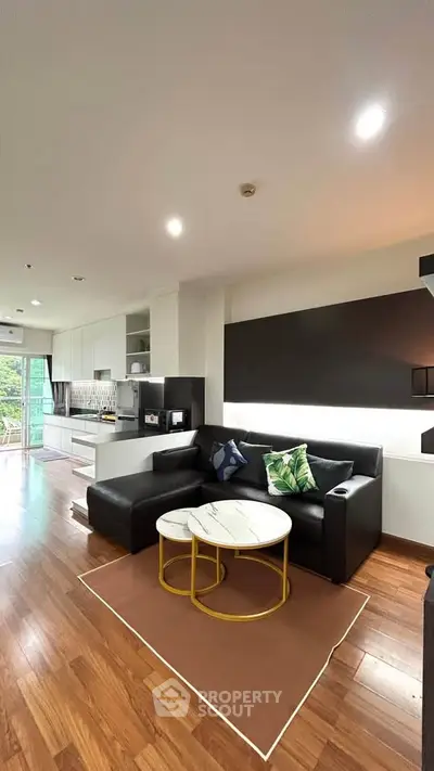 Modern living room with sleek black sofa, stylish decor, and open kitchen layout in a contemporary apartment.