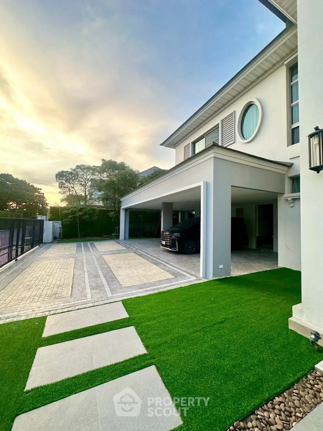 Luxurious modern house with spacious driveway and lush green lawn at sunset.