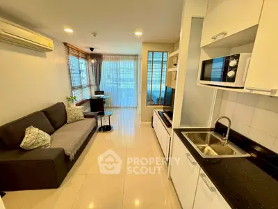 Modern living room with open kitchen, featuring sleek appliances and cozy seating area.