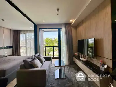 Modern living room with sleek design and large TV, featuring a view of the balcony and greenery.