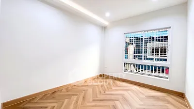Spacious empty room with elegant herringbone wooden flooring and large window.