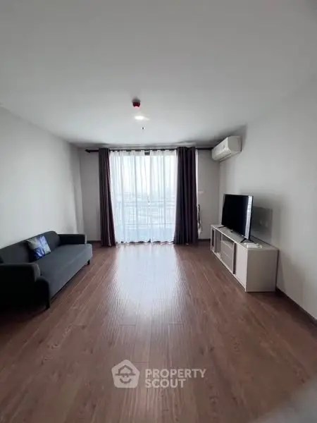 Spacious living room with wooden flooring and large window for natural light.