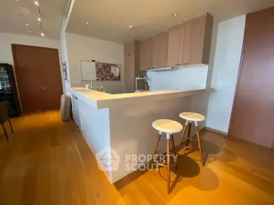 Modern kitchen with sleek design and wooden flooring, featuring a breakfast bar and stylish stools.