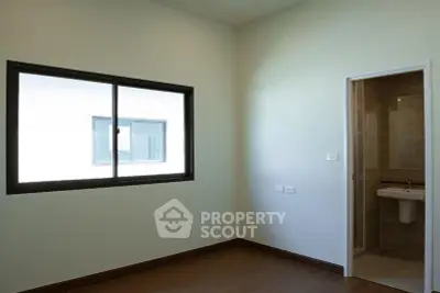Spacious bedroom with ensuite bathroom and large window in modern apartment.