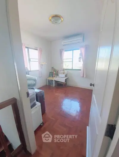 Cozy bedroom with wooden flooring and natural light, featuring air conditioning and a serene atmosphere.