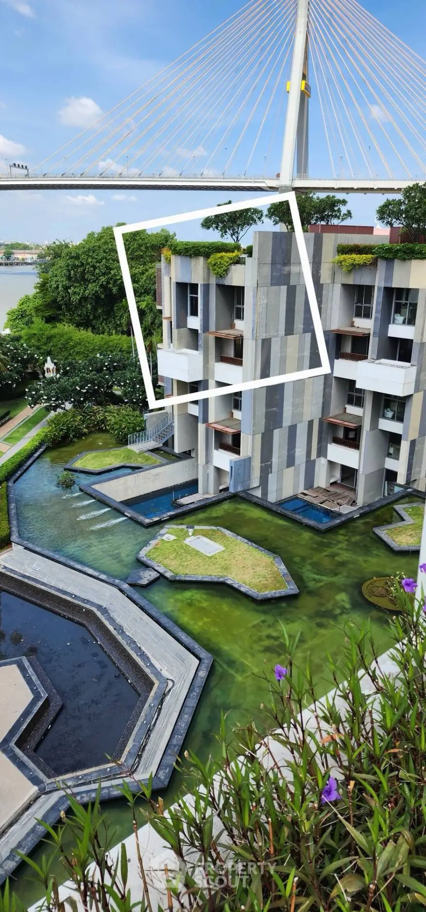 Modern building with unique architecture and lush greenery near a river, featuring a striking bridge in the background.