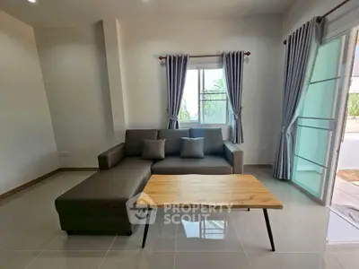 Modern living room with sleek sofa and wooden coffee table, featuring natural light and stylish curtains.