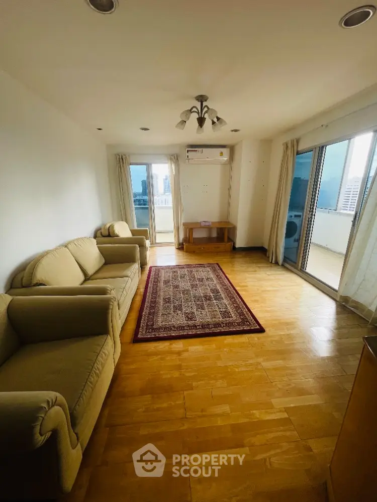 Spacious living room with balcony and city view, featuring cozy sofas and elegant wooden flooring.