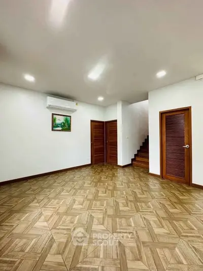 Spacious living room with wooden flooring and modern lighting, featuring a staircase and air conditioning.
