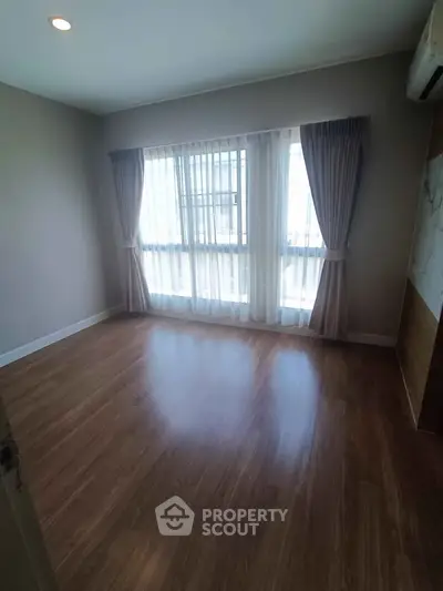 Spacious empty bedroom with large window and wooden flooring