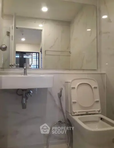 Modern bathroom with sleek fixtures and marble walls, featuring a toilet and sink.