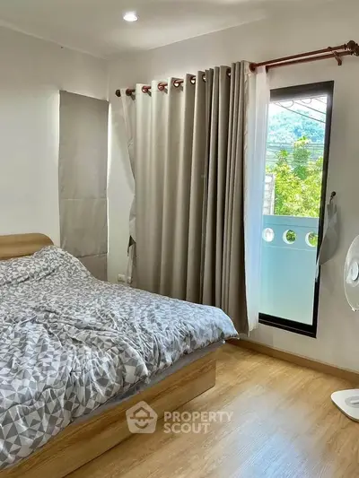 Cozy bedroom with wooden flooring and large window overlooking greenery
