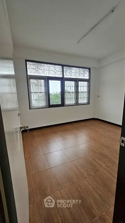 Spacious empty room with large window and tiled flooring, perfect for customization.
