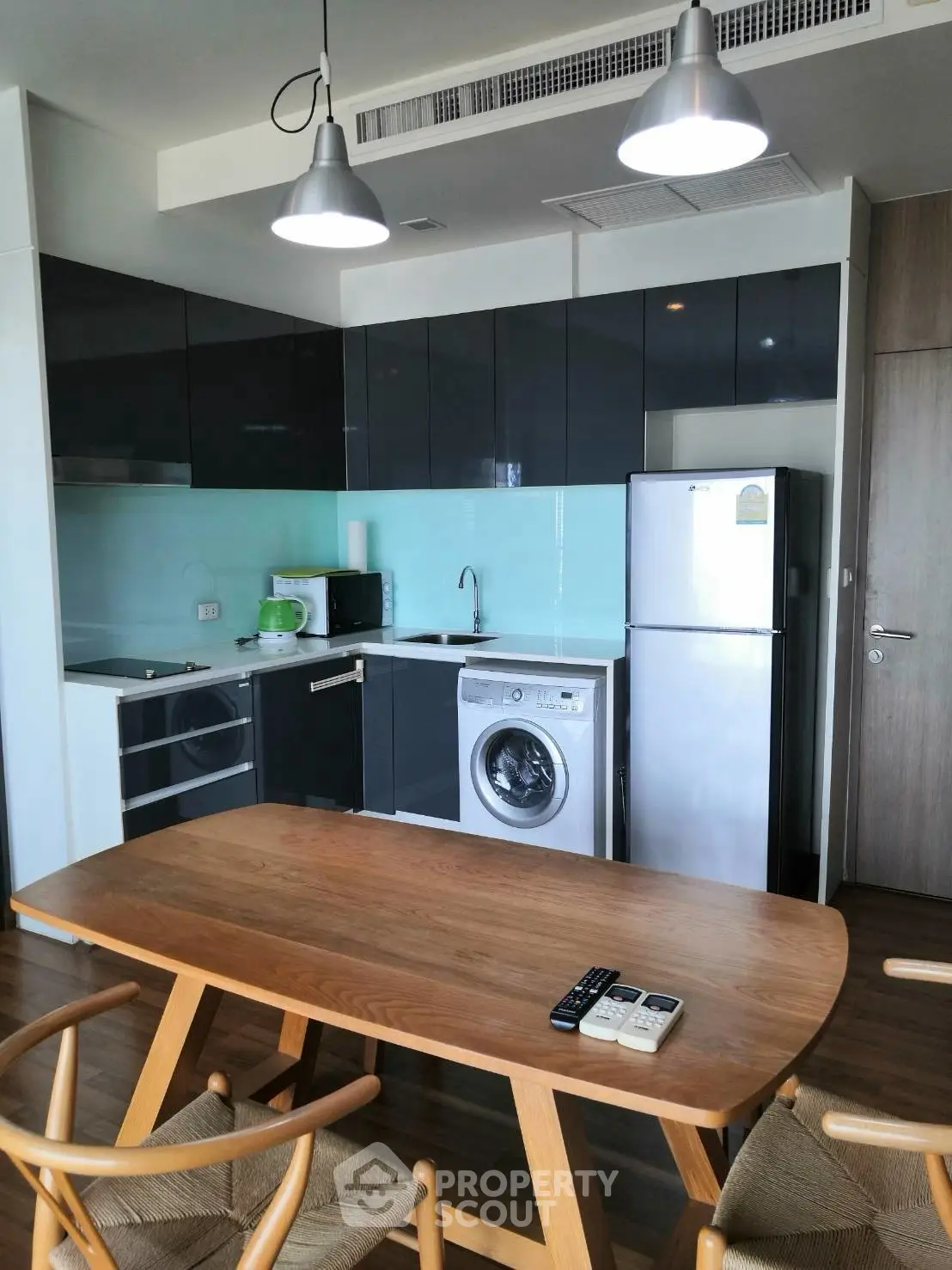 Modern kitchen with sleek cabinets, washing machine, and dining table in stylish apartment.