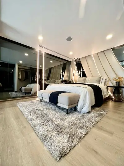 Luxurious bedroom with plush king-sized bed, elegant lighting, and mirrored wardrobe, featuring a cozy shag rug and modern accents.
