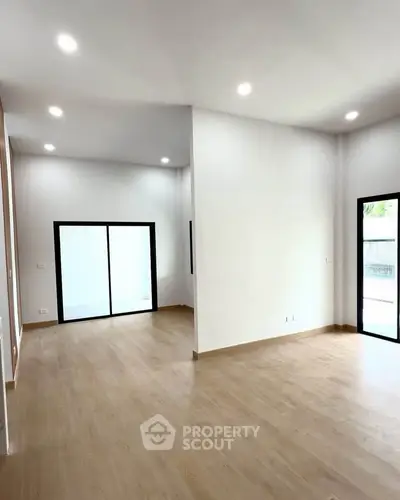 Spacious modern living room with wooden flooring and large windows for natural light.