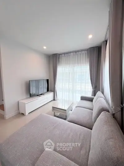 Modern living room with large sofa and TV, featuring floor-to-ceiling windows and elegant curtains.