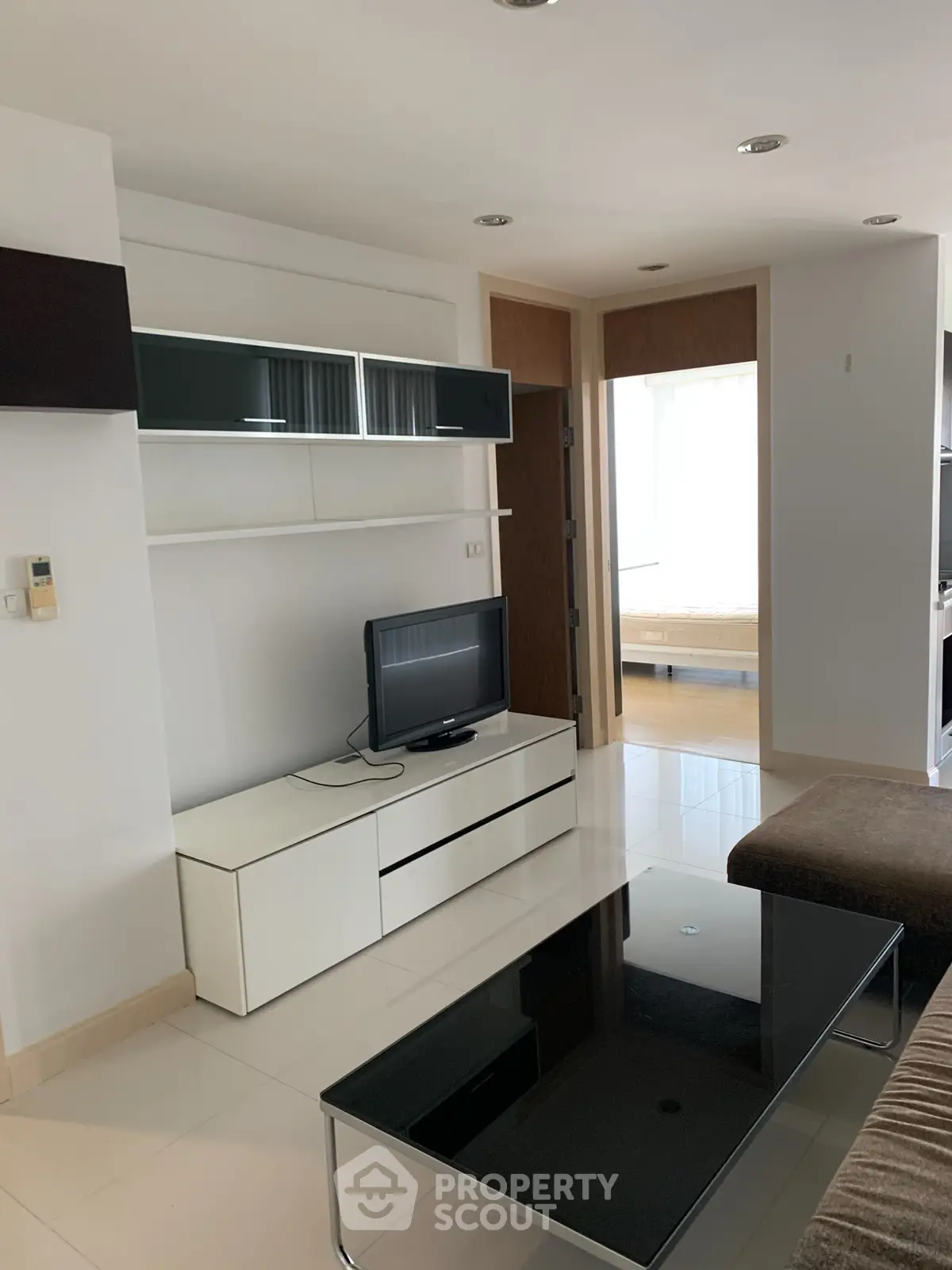 Modern living room with sleek furniture and open layout, leading to a bright bedroom.