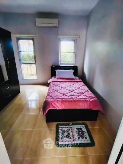 Cozy bedroom with single bed, air conditioning, and natural light from two windows.