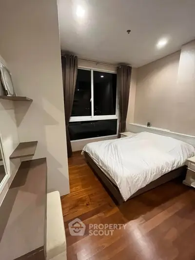 Modern bedroom with wooden flooring and large window, featuring cozy lighting and elegant decor.