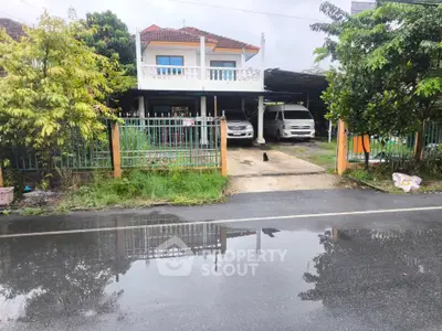 Charming two-story house with balcony and carport, surrounded by lush greenery, perfect for family living.