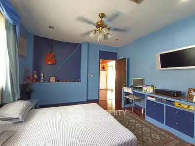 Charming blue bedroom with ceiling fan, wall-mounted TV, and cozy workspace.