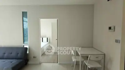 Modern apartment interior with minimalist furniture and neutral tones, featuring a cozy living area and a glimpse of the bedroom.