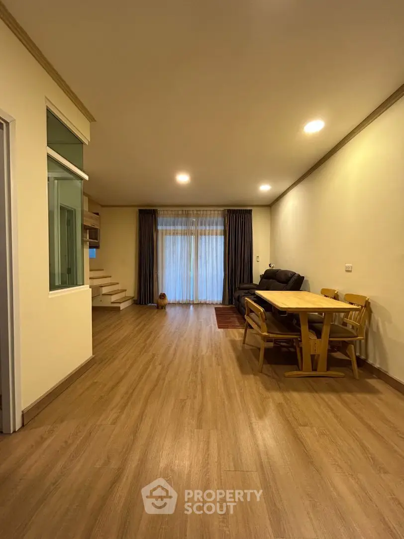 Spacious living room with warm wooden flooring, ample natural light, and a cozy dining area, perfect for family gatherings and relaxation.