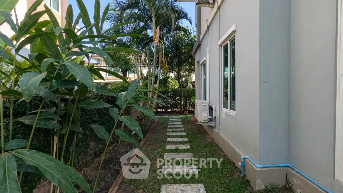 Charming garden pathway beside modern home with lush greenery and large windows.