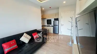 Modern living room with sleek furniture and compact kitchen area in open layout apartment.
