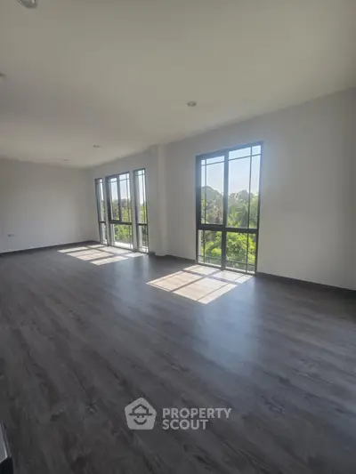 Spacious sunlit living room with large windows and modern flooring, offering serene garden views.