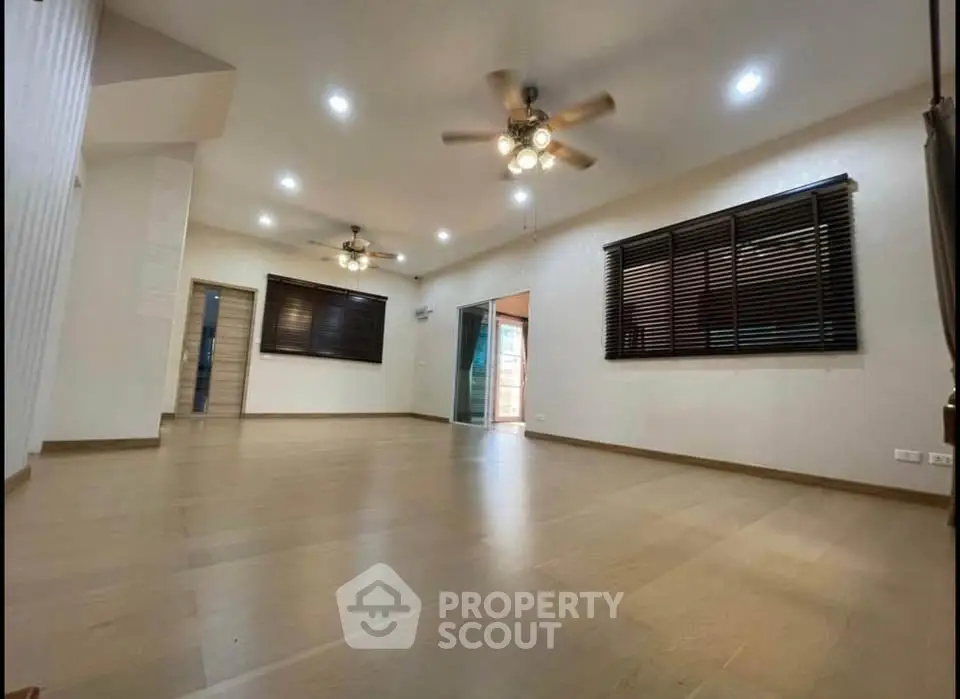 Spacious living room with wooden flooring and ceiling fans, ideal for family gatherings.