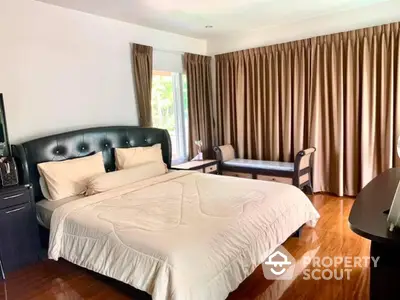 Elegant master bedroom with polished hardwood floors and expansive windows draped in luxurious curtains, featuring a large bed with a tufted headboard.