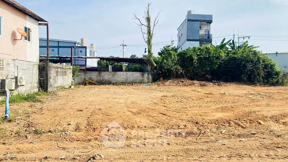 Vacant land plot ready for development in a suburban area with nearby houses.