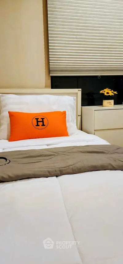 Cozy bedroom with stylish decor and bright orange accent pillow, perfect for relaxation and comfort.