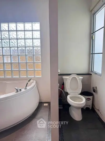 Modern bathroom with glass block window and separate toilet area, featuring a sleek bathtub.