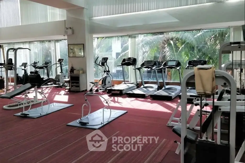 Spacious gym with modern equipment and large windows offering lush greenery views.