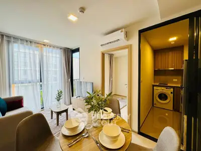 Modern apartment interior with open living area, dining table, and kitchen featuring washing machine.