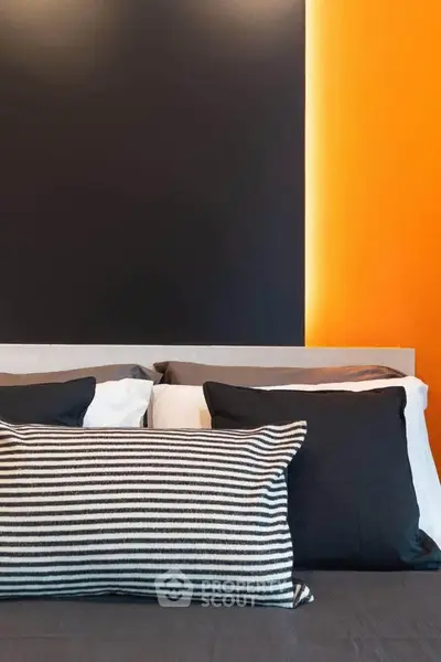 Modern bedroom with stylish black and orange accent wall and cozy pillows.