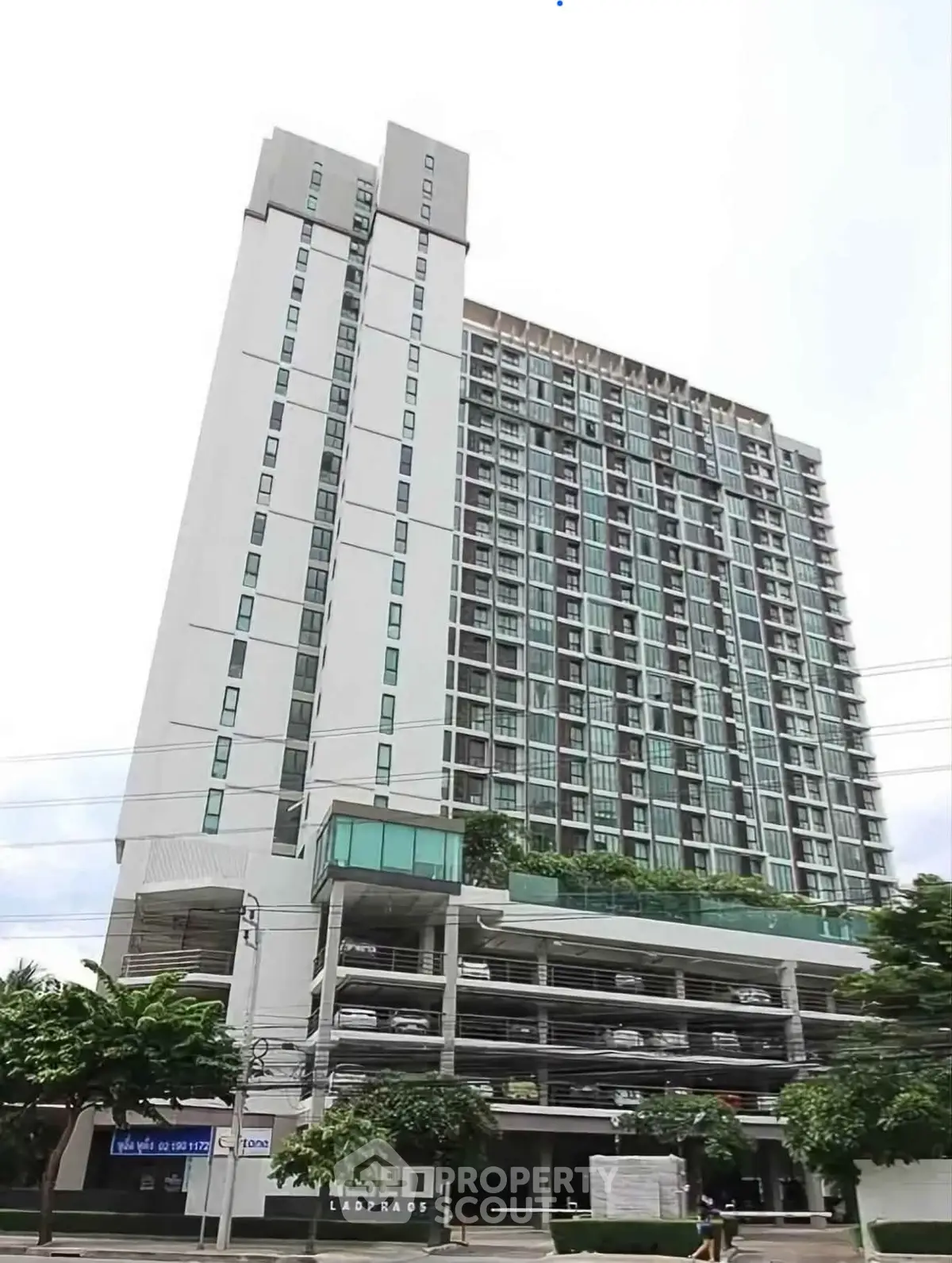 Modern high-rise condominium with parking garage and lush greenery in urban setting.
