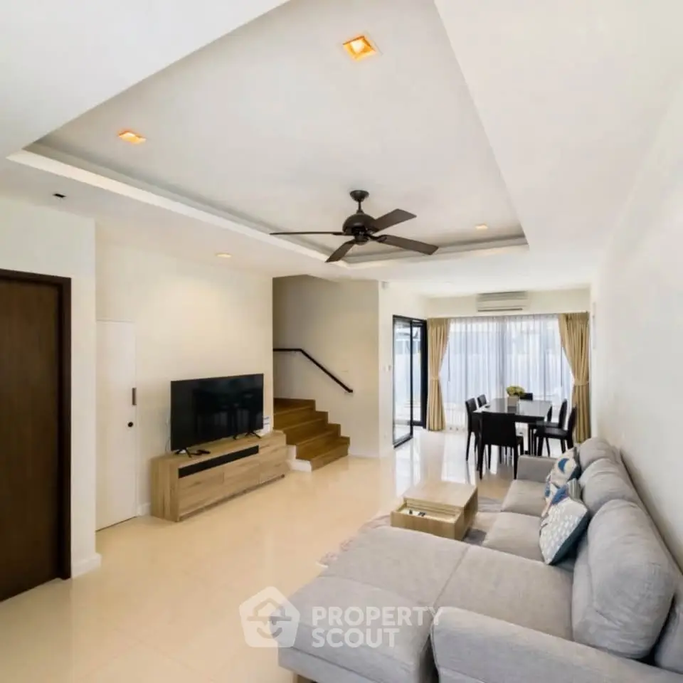 Spacious living room with modern decor and open dining area, featuring a cozy sofa and large windows.