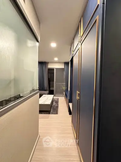 Modern apartment hallway with elegant blue cabinetry and cozy living area leading to a balcony.
