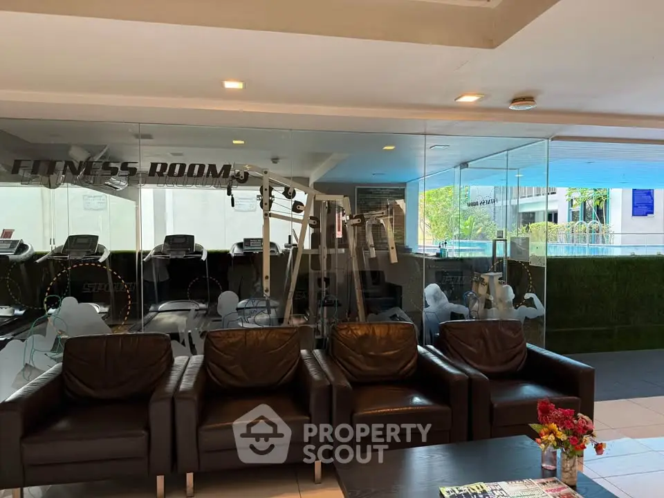 Modern fitness room with glass walls and leather seating in upscale residential building.