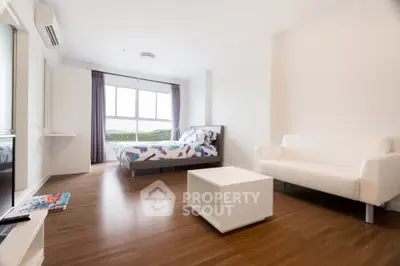 Modern studio apartment with wooden flooring, featuring a cozy bed and a sleek white sofa.